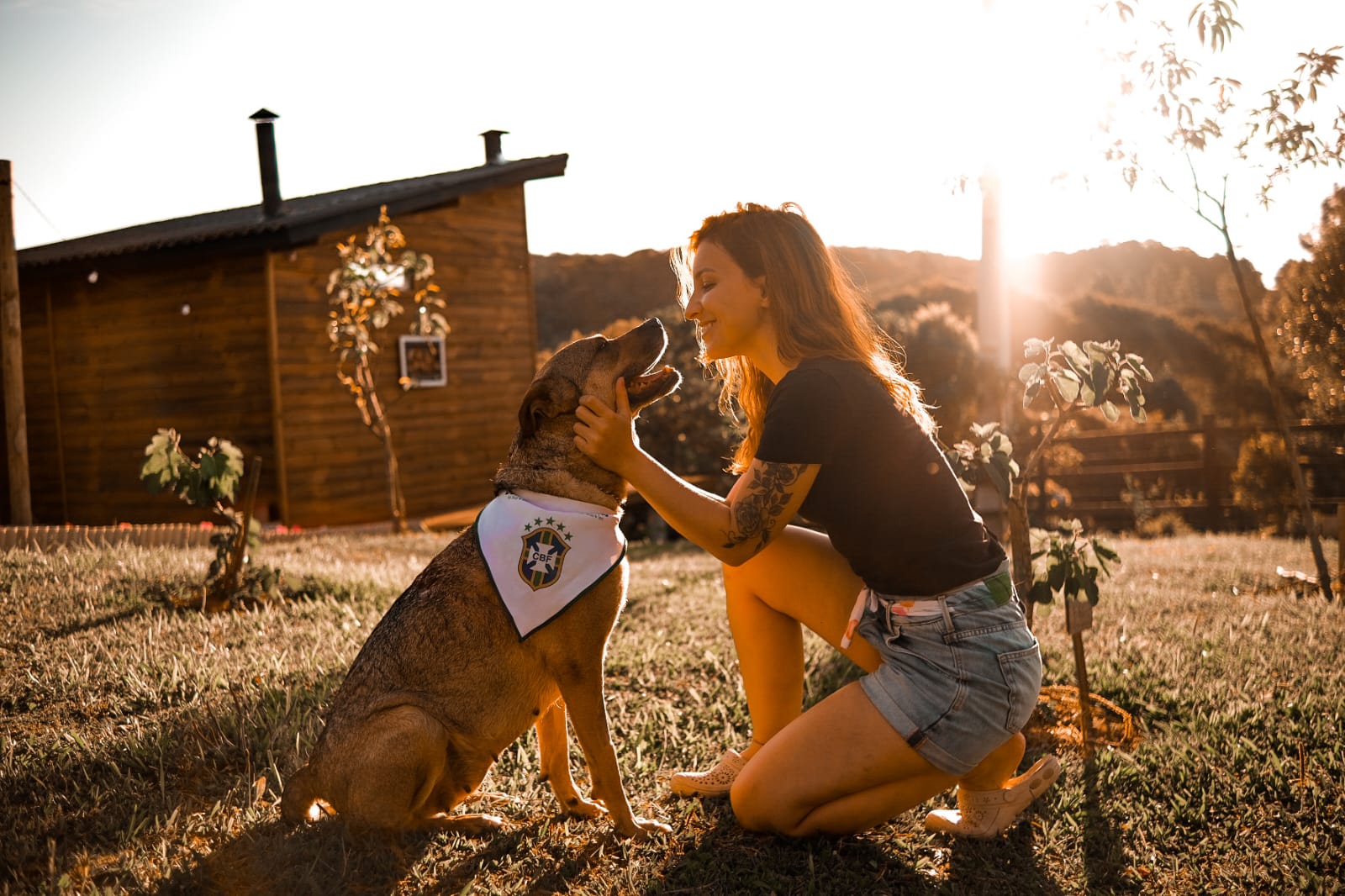Hóspede com cachorro no jardim do chalé ao pôr do sol