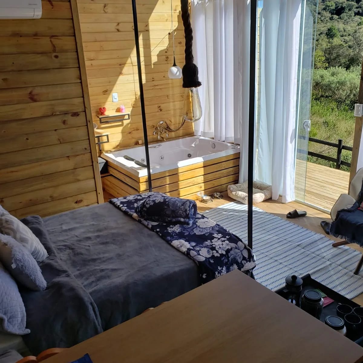 Interior aconchegante do chalé com hidromassagem junto à cama e vista para o verde